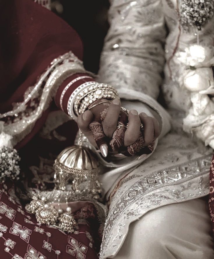 Luxury bridal ceremony close-up of couple holding hands with detailed henna and gold jewelry.